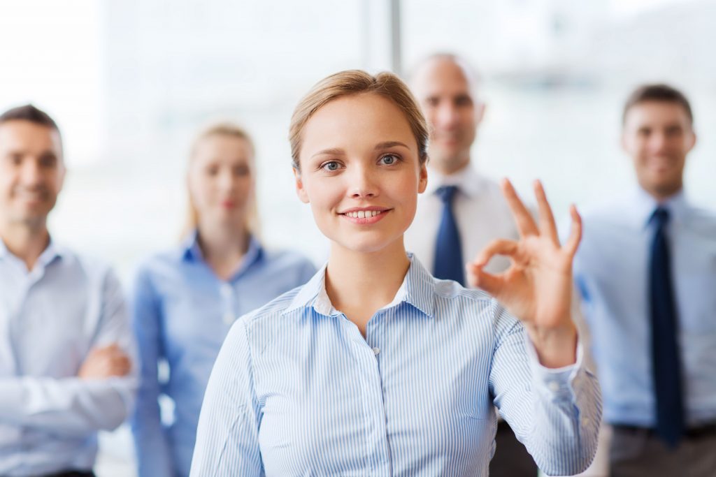 business, people, gesture and teamwork concept - smiling businesswoman showing ok sign with group of businesspeople in office